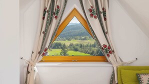 Ein Fenster mit Blick auf eine grüne Landschaft und Berge, eingefasst von einem Holzrahmen und mit Vorhängen verziert.