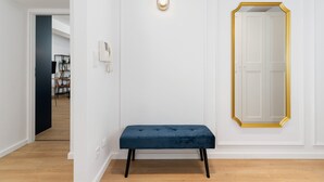 A hallway with a dark blue bench, a wall-mounted light fixture, and a door with a gold frame. - Elegant Apartment | Close to Market | Place to Work (Kraków)
