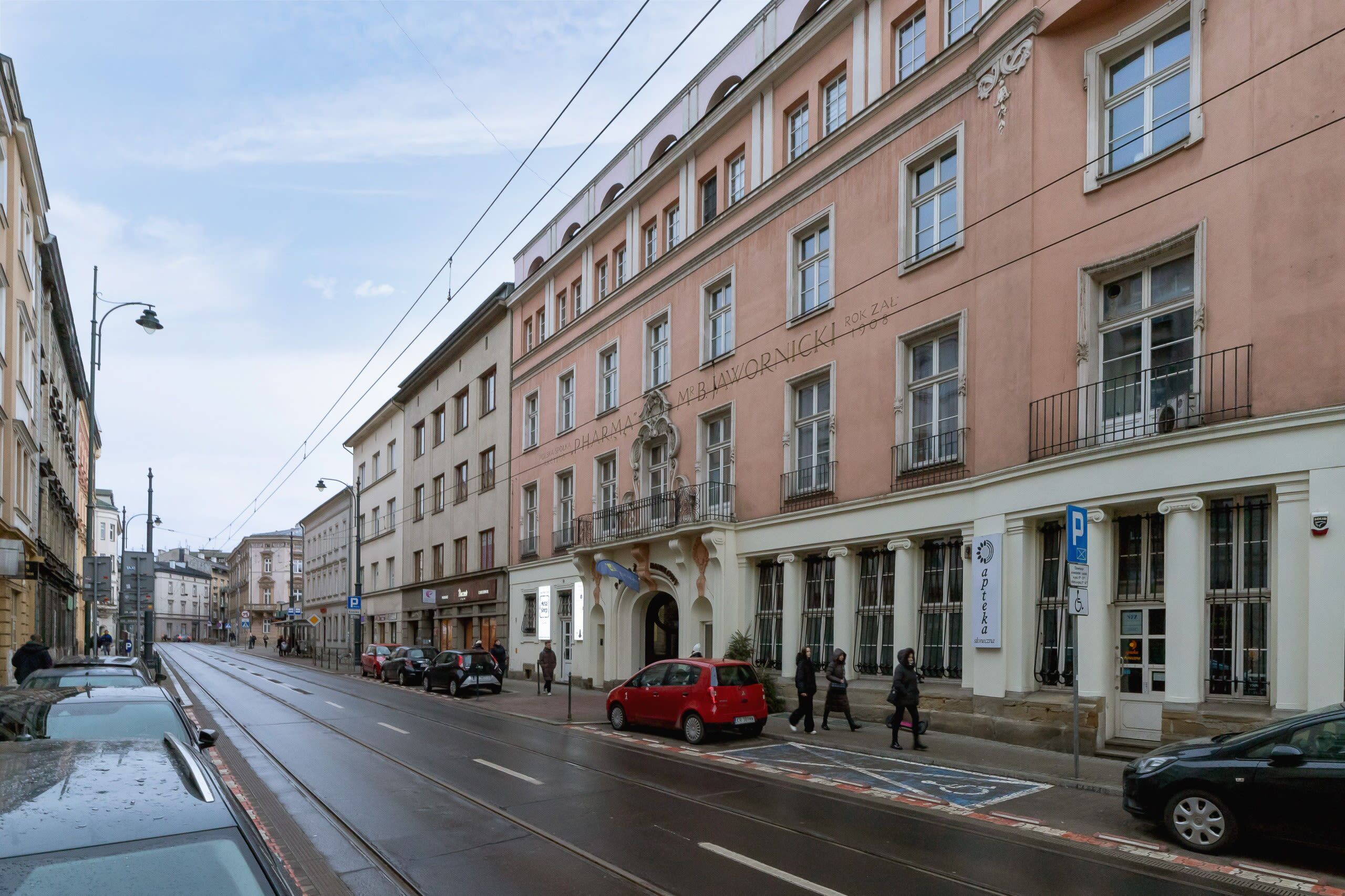 Straßenansicht mit Straßenbahnlinie, einem roten Auto, das am Straßenrand geparkt ist, und einem Gebäude mit dem Schild 'Hotel M. B. M. BAWORNICKI'.