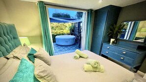 A neatly made bed with pillows and towels, a blue ottoman, and a dresser with a mirror. - A Hidden Gem With Private Hot Tub and Garden (Bournemouth)