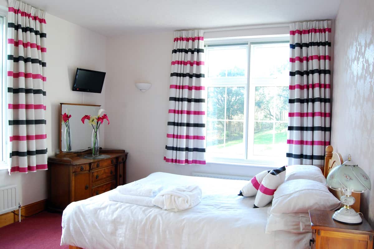 A bedroom with a large bed, a dresser, a TV mounted on the wall, and a window with curtains.