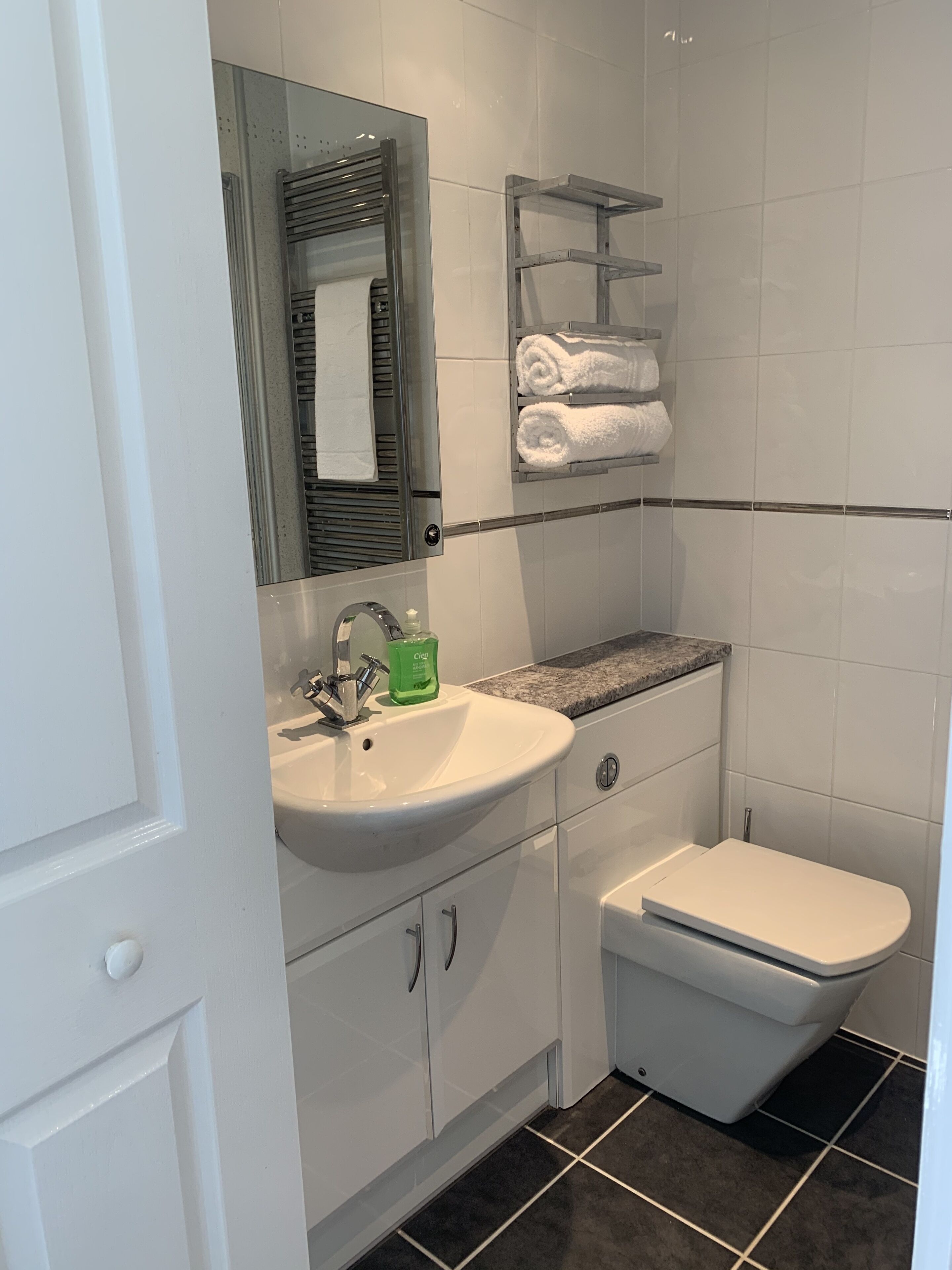 A modern bathroom with a white sink, a mirror, a toilet, and a towel rack.