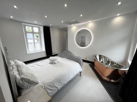 A modern bedroom with a bed, a round mirror, and a freestanding bathtub.