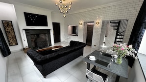 Uma sala de estar moderna com um sofá preto, uma mesa de jantar com um vaso de flores e uma lareira.