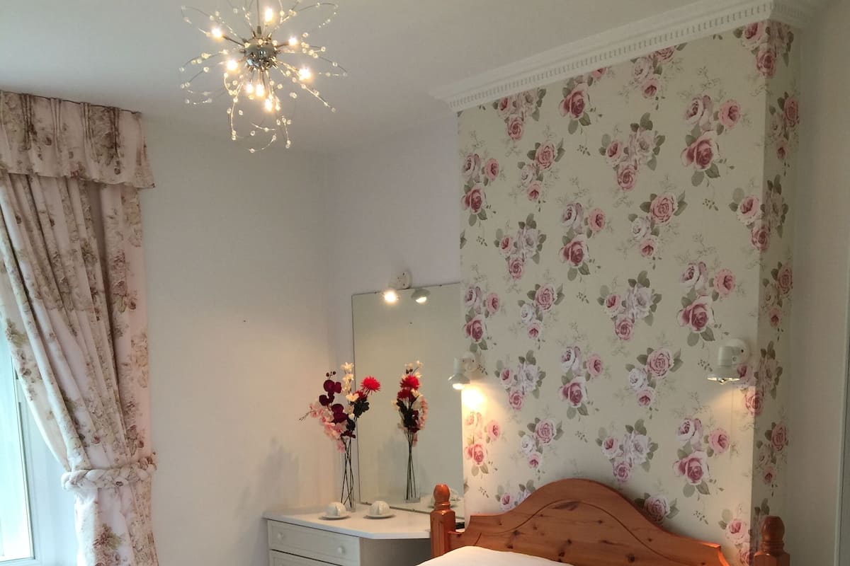 A bedroom with a wooden bed, a mirror, a dresser, and floral wallpaper.