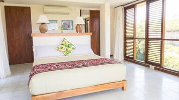 A spacious bedroom with a large bed, wooden headboard, and a view through floor-to-ceiling windows.