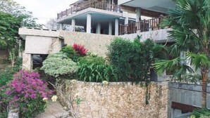 A multi-story building with a stone facade, balconies, and a garden area with various plants and flowers. - Adila Bali (Ungasan)