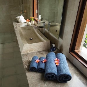 A modern bathroom with a large bathtub, a sink, and a mirror. There are towels and a bottle of soap on the counter.