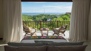 A balcony with a bed, two chairs, and a small table. - Adila Bali (Ungasan)