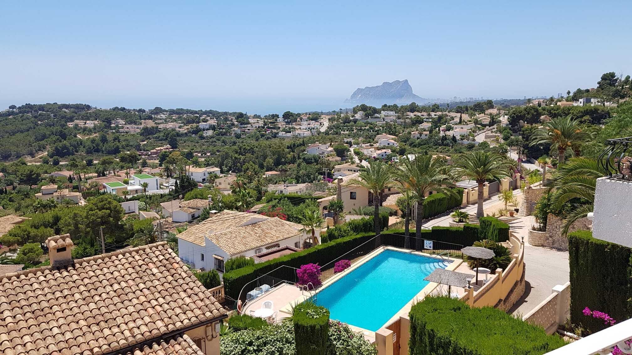 A residential area with a swimming pool, surrounded by houses and greenery, overlooking a coastal landscape.