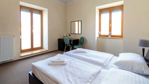 A hotel room with two beds, a desk, a chair, a window, and a radiator. - Hotel Prácheň (Horazdovice)