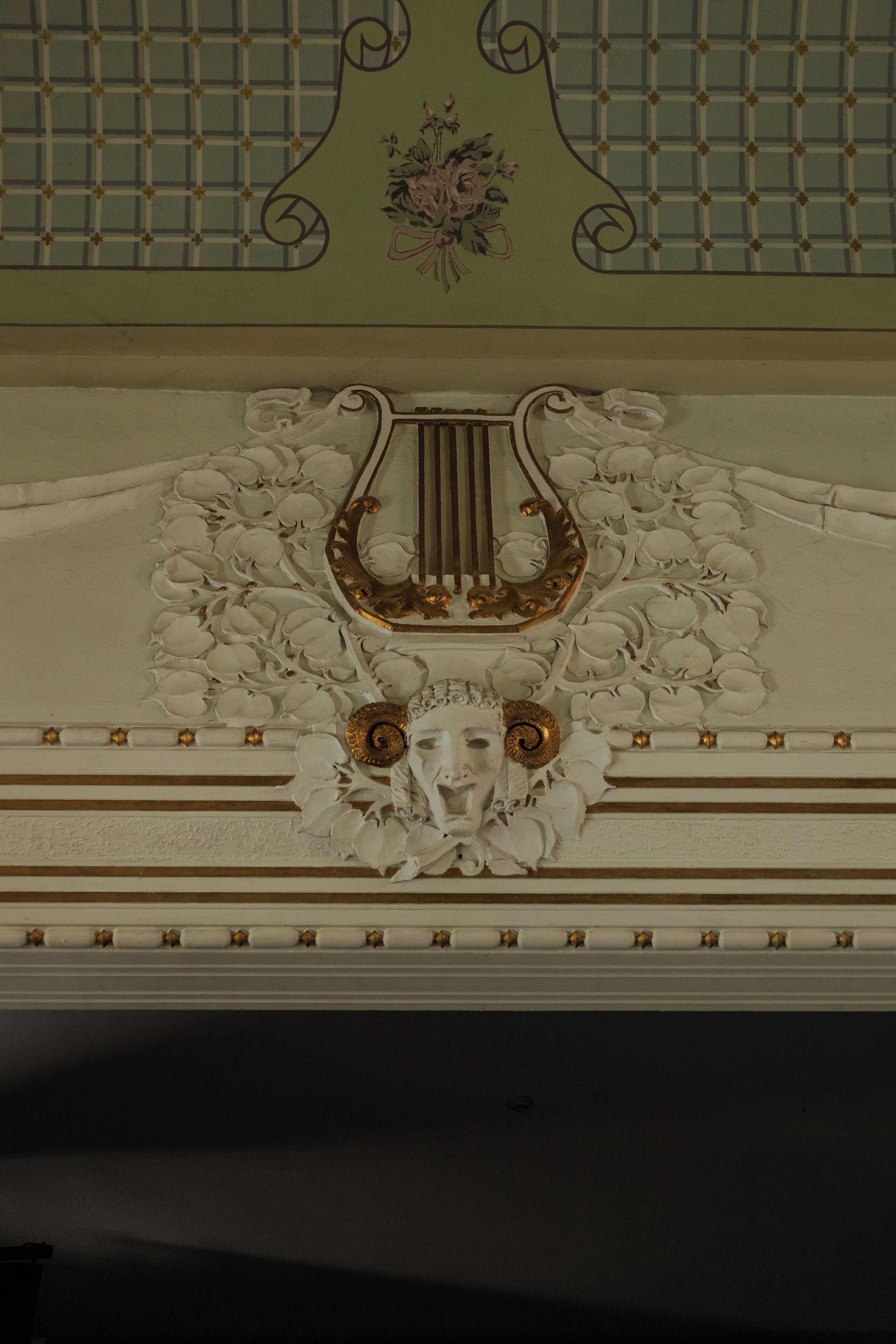 Un plafond architectural richement décoré, orné de motifs floraux et géométriques complexes, et comprenant un élément décoratif central rappelant une lyre.