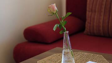 Una mesita pequeña con un florero que contiene una sola flor, un control remoto y una revista.