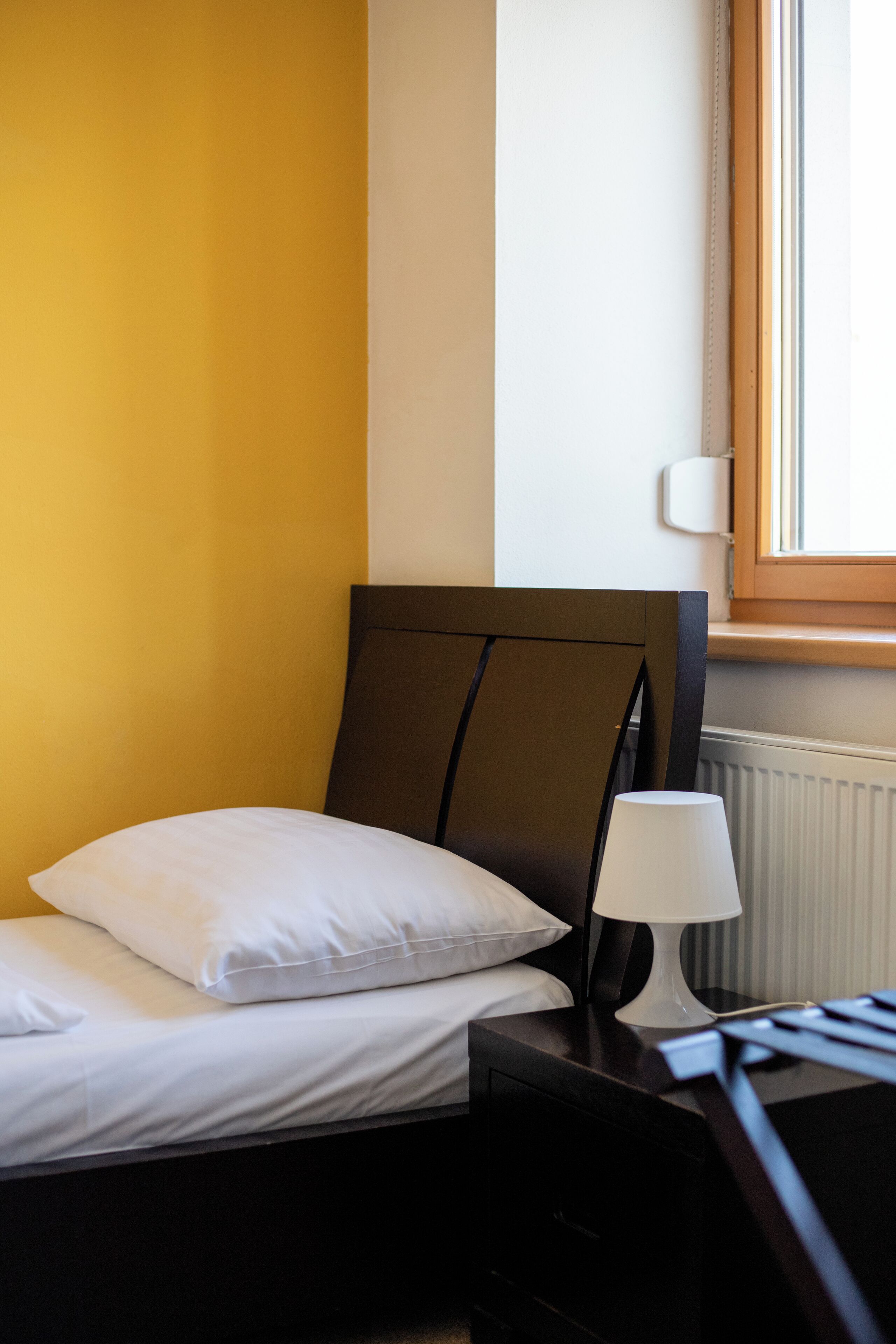 Una cama bien tendida con ropa blanca, un cabecero de madera oscura y una mesita de noche con una lámpara blanca.