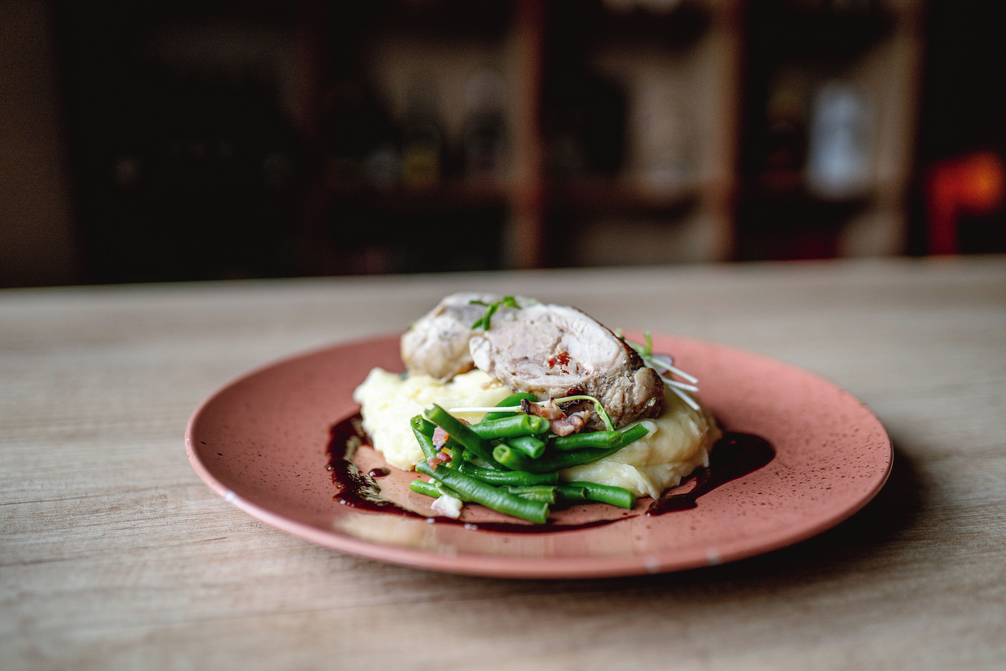 A plate of food with a slice of meat, green beans, and mashed potatoes on a pink plate.