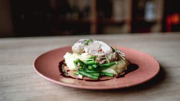 A plate of food with a slice of meat, green beans, and mashed potatoes on a pink plate.