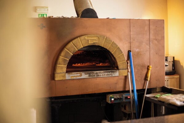 Un horno de ladrillo con una pizza en su interior, un trapeador y una herramienta de limpieza.