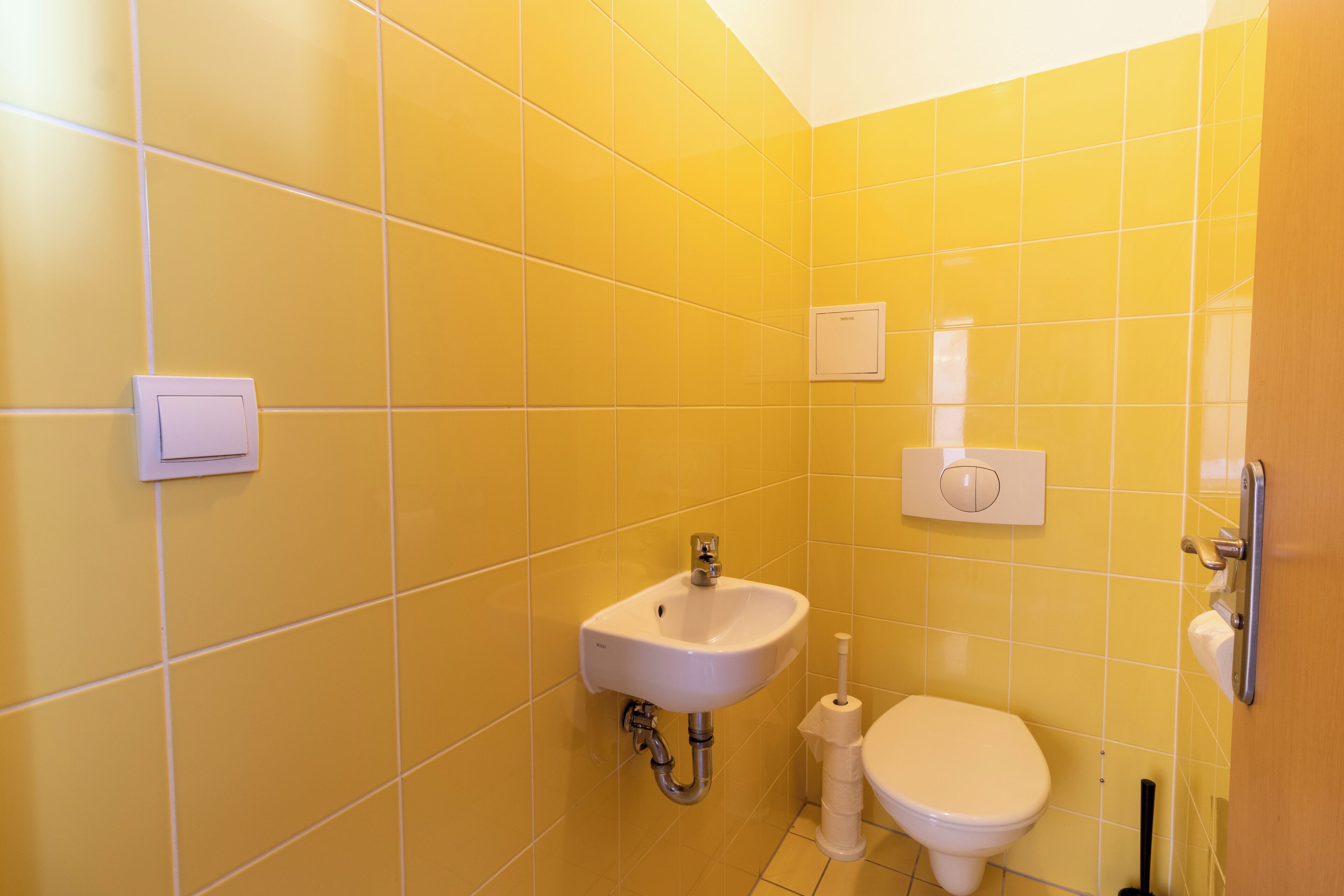 A bathroom with yellow tiles, a white sink, a toilet, and a hand dryer.