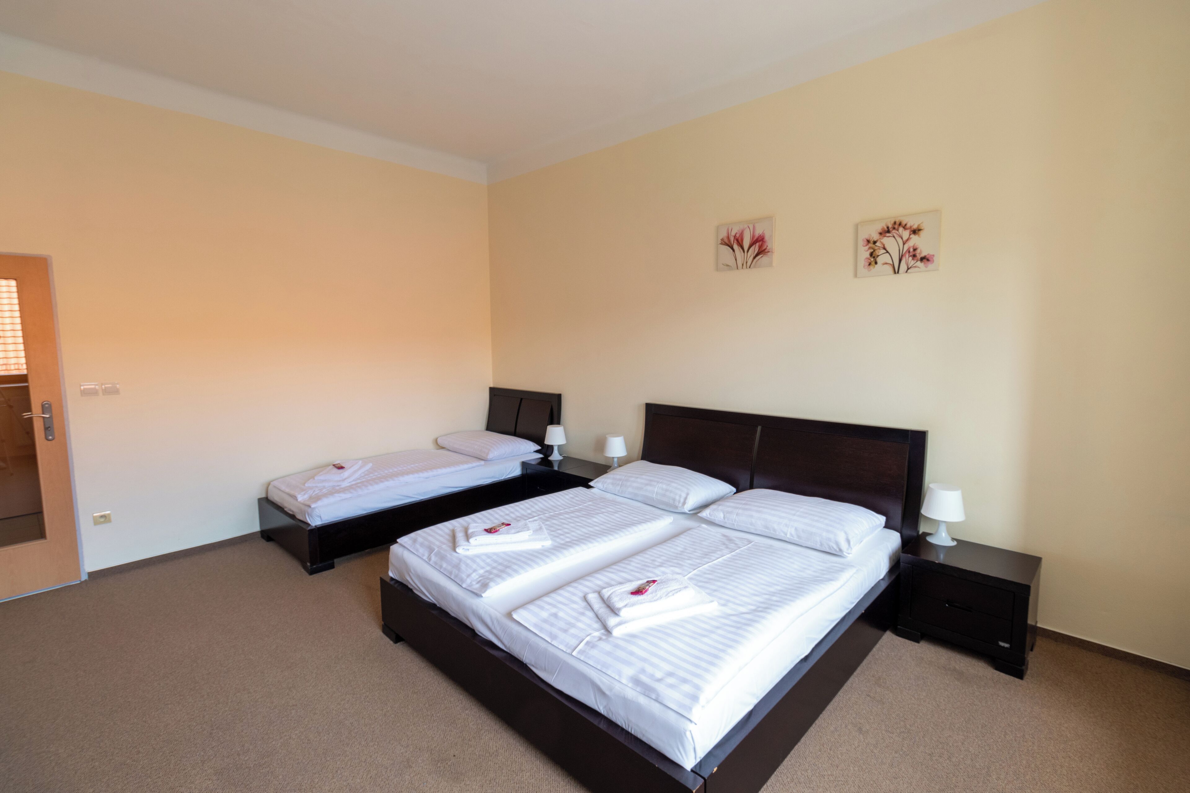 A hotel room with two beds, each with white linens and towels, a dark wooden headboard, bedside tables with lamps, and a door with a handle.