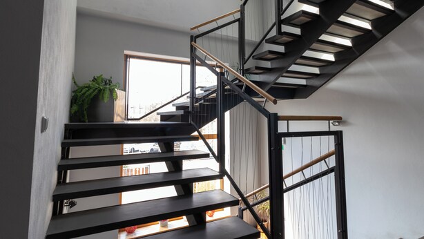 A modern staircase with black railings and wooden handrails, leading to an upper floor. - Hotel Prácheň (Horazdovice)