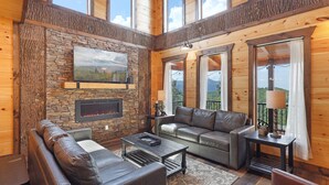 A cozy cabin interior with a stone fireplace, leather sofas, and large windows offering a view of the outdoors. - Paradise Pool Lodge, Private Indoor Pool, $560 FREE tickets each paid day!!! (Sevierville)