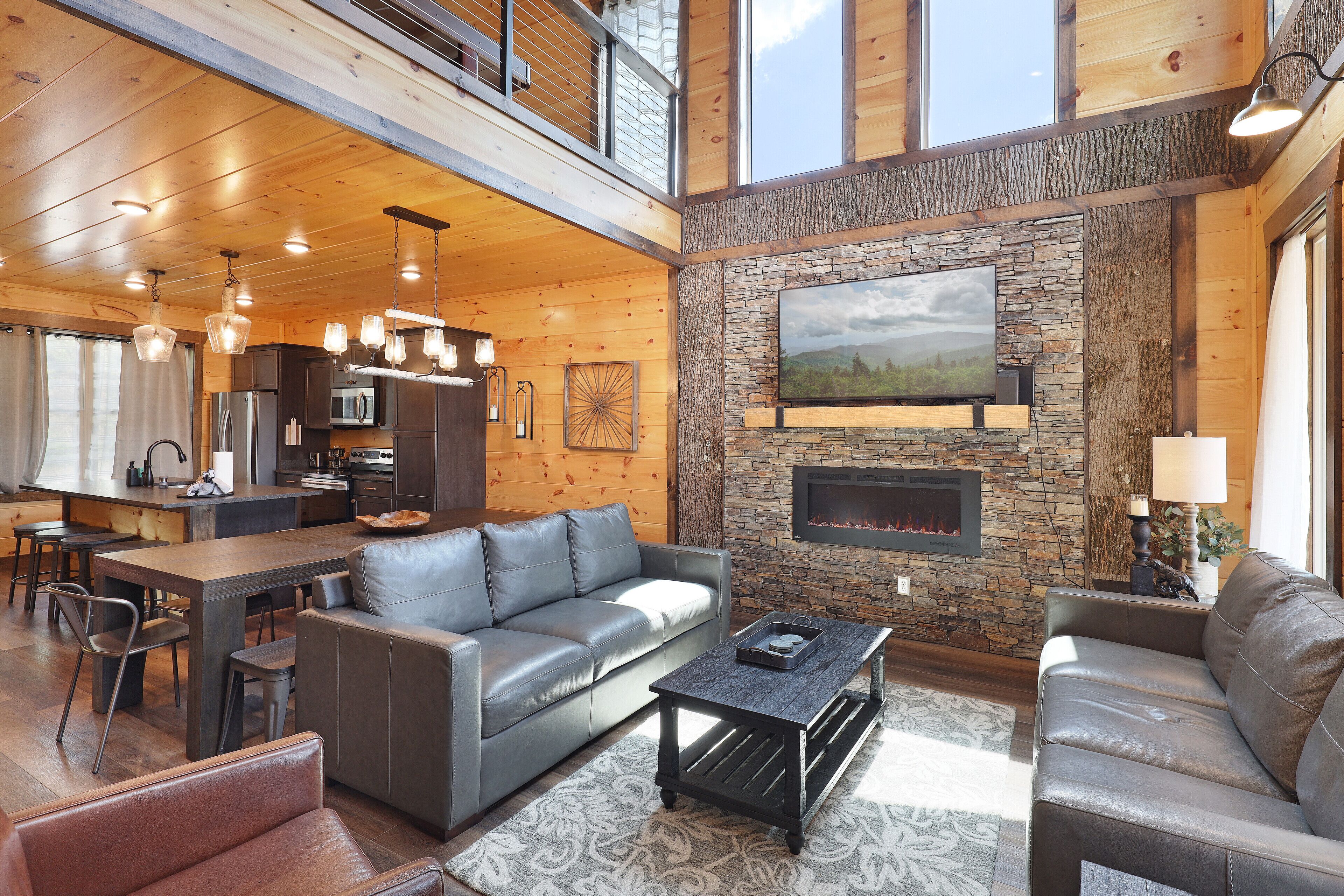 A spacious living area with a fireplace, leather sofas, and a dining area with a kitchen in the background.
