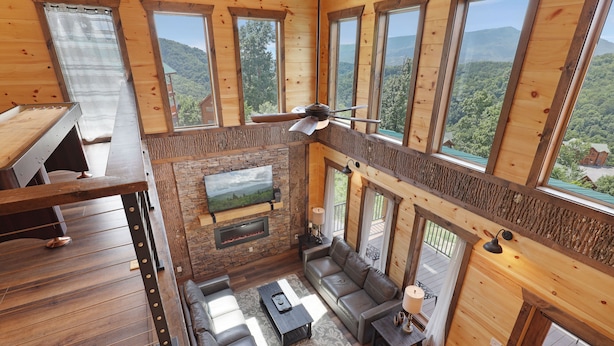 A spacious loft-style living area with a fireplace, large windows, and a view of the surrounding forest. - Paradise Pool Lodge, Private Indoor Pool, $560 FREE tickets each paid day!!! (Sevierville)