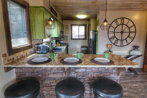 A kitchen with granite countertops, green cabinets, a large clock, and a stone island with bar stools. - Paradise Vista - Hot Tub, Resort Pool, AWESOME Mtn. Views, Free Tickets! (Gatlinburg)