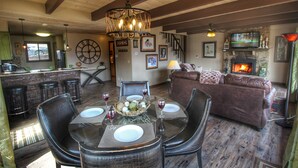 Uma sala de estar acolhedora com lareira, uma mesa de jantar posta para quatro e um espaço bar com banquetas.