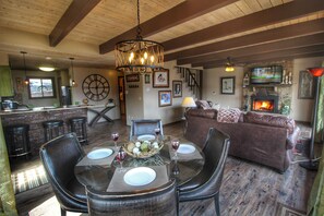 A cozy living area with a fireplace, a dining table set for four, and a bar area with stools. - Paradise Vista - Hot Tub, Resort Pool, AWESOME Mtn. Views, Free Tickets! (Gatlinburg)
