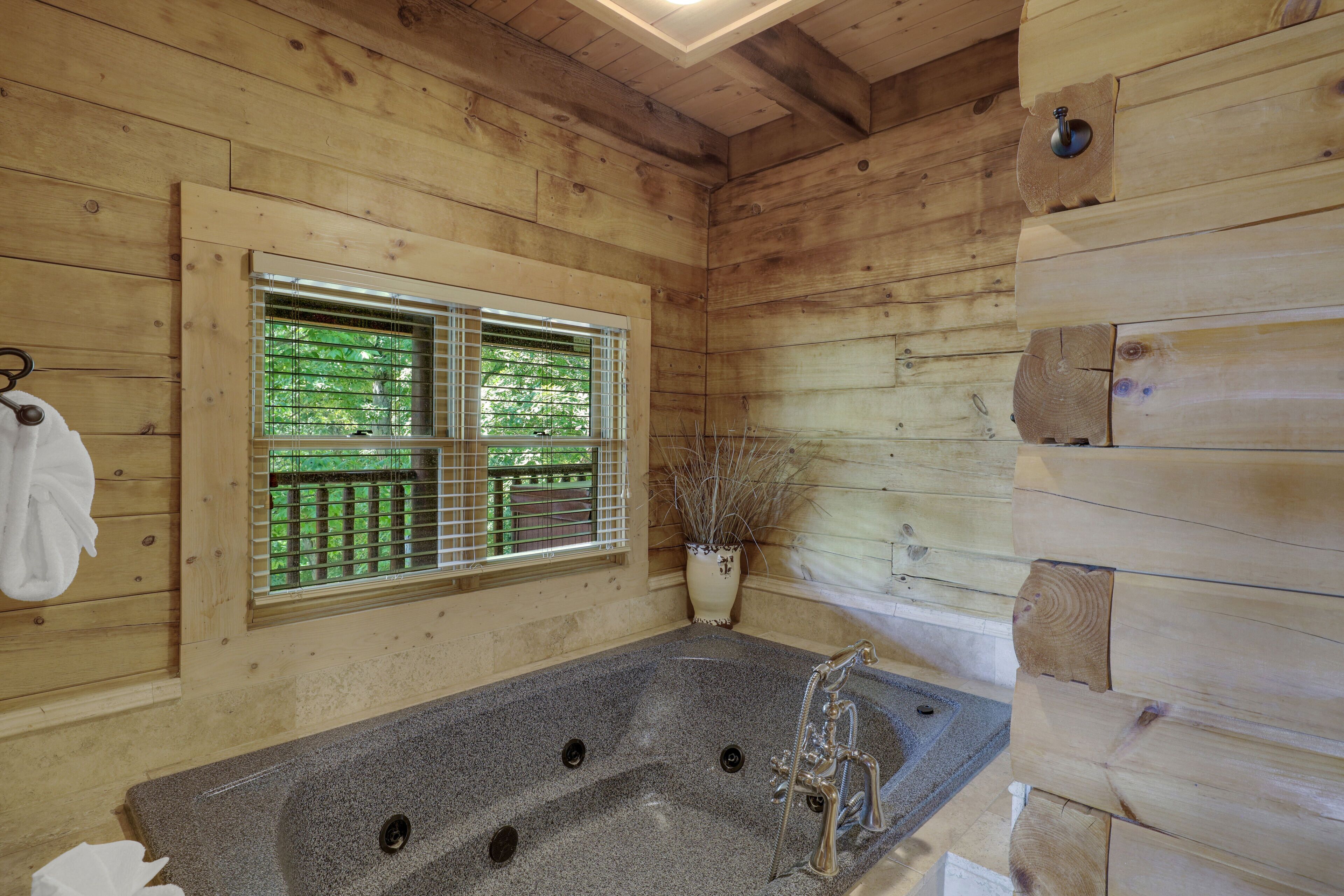 Ein Interieur einer Holzhütte mit einer Steinbadewanne, einem Fenster mit Jalousien und einem Blumentopf.
