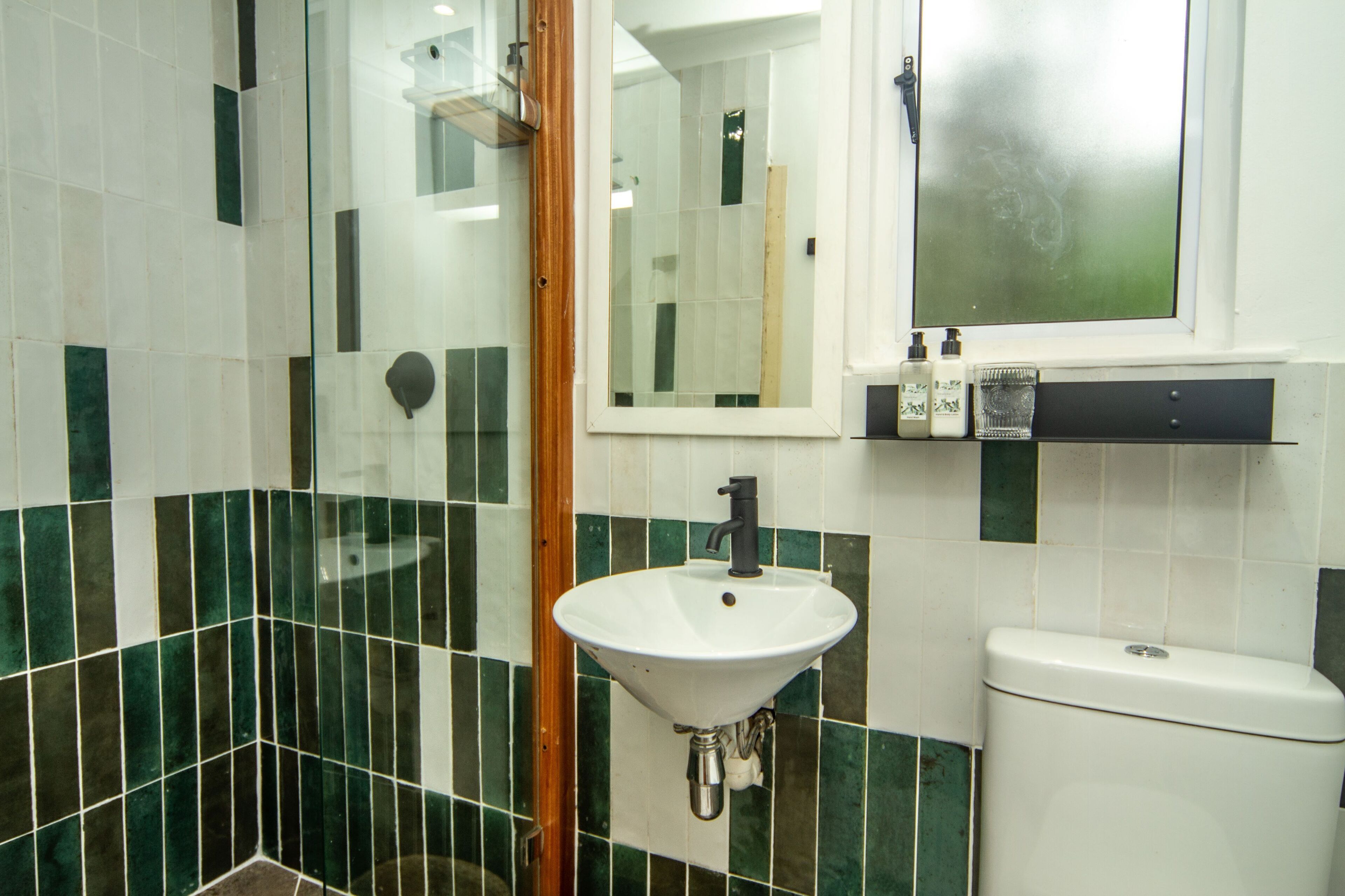 A bathroom with a white sink, green and white tiles, a mirror, and a toilet.