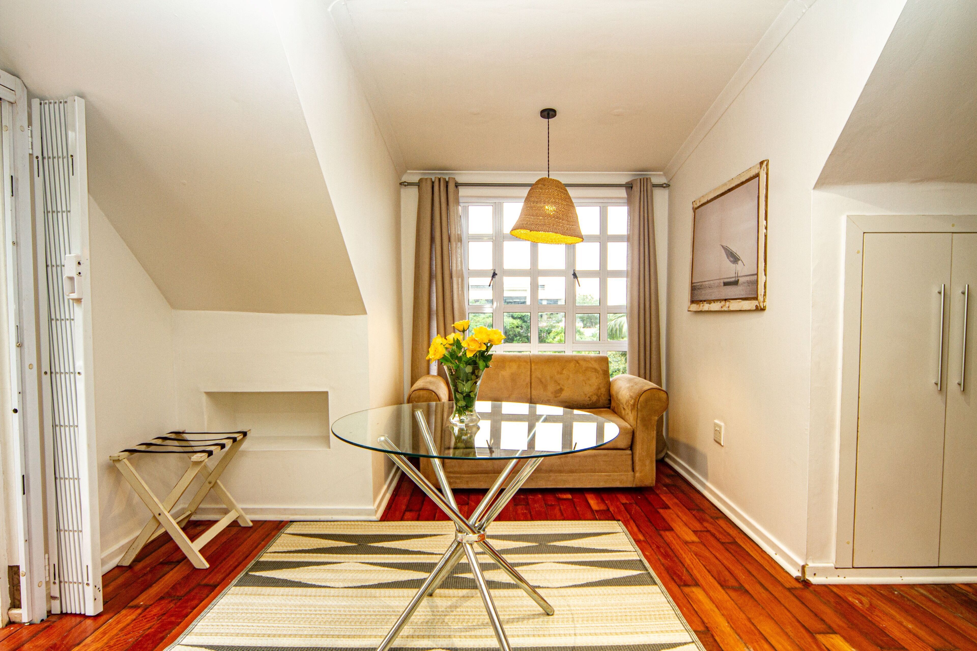 A room with a glass table, a sofa, a window with curtains, and a framed picture on the wall.