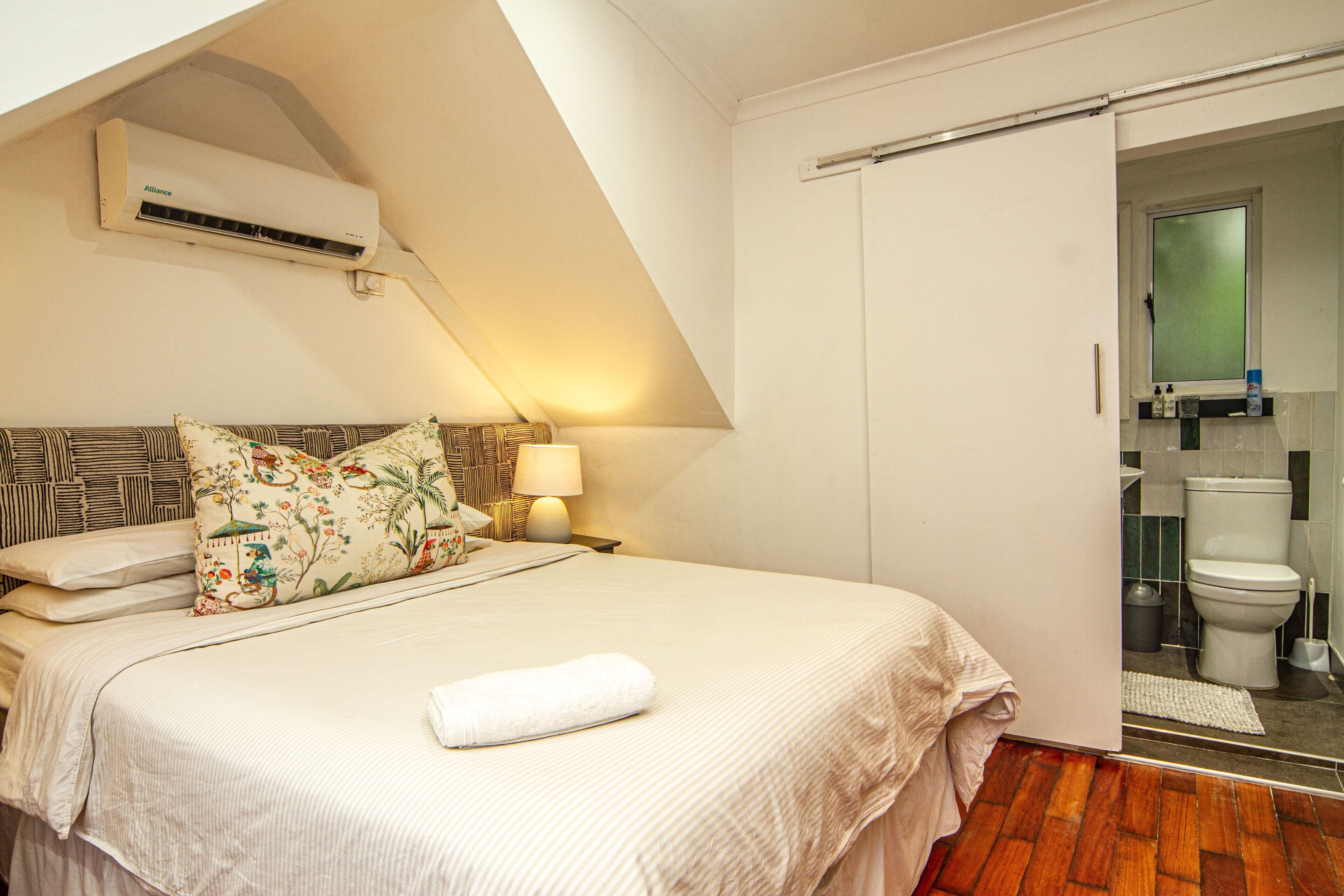 A bedroom with a bed, pillows, a bedside lamp, and an air conditioning unit on the wall.