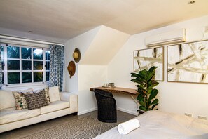 A bedroom with a bed, a sofa, a chair, a large plant, and artwork on the walls.