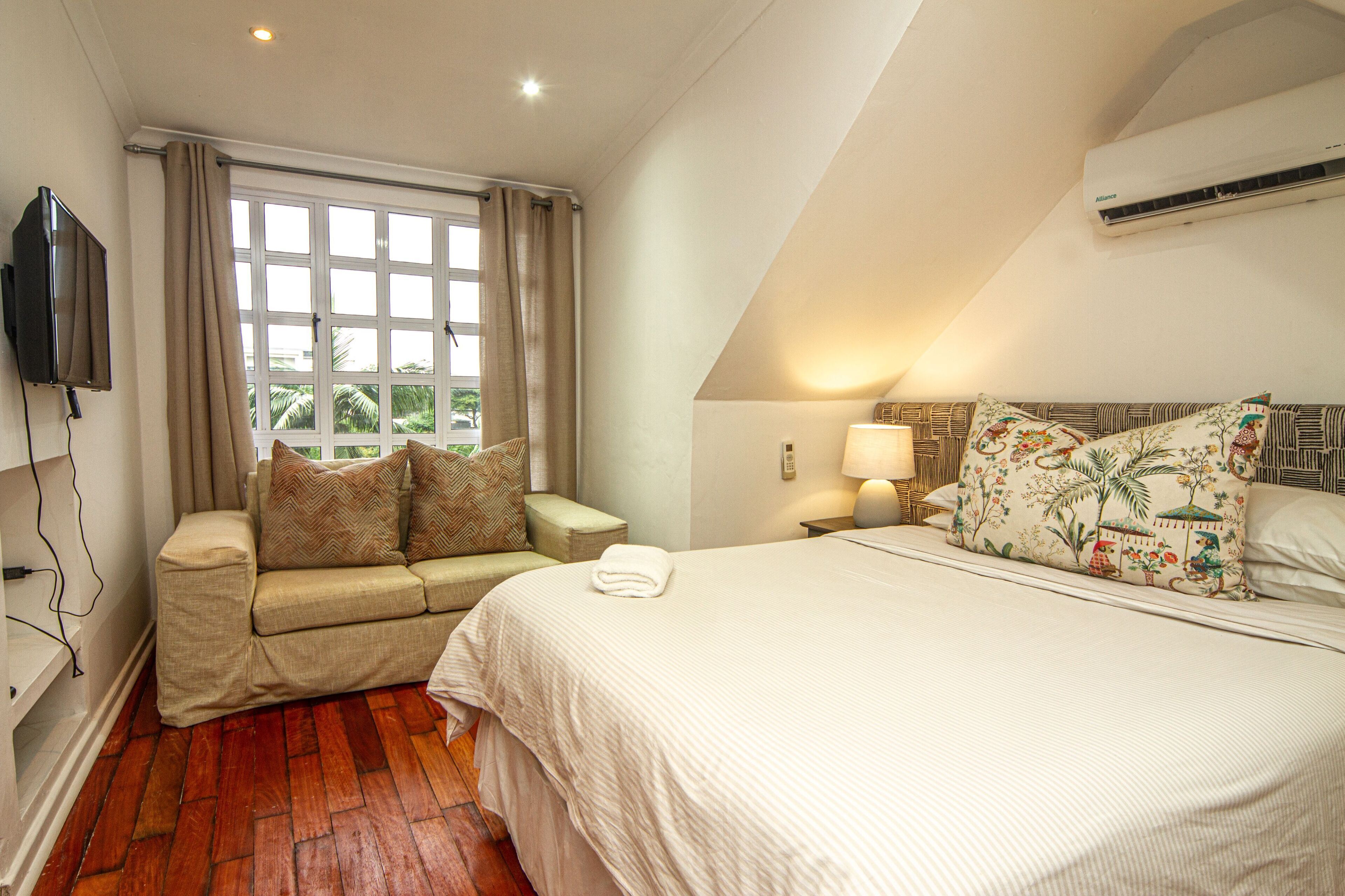 A bedroom with a bed, a sofa, a TV, and a window with curtains.