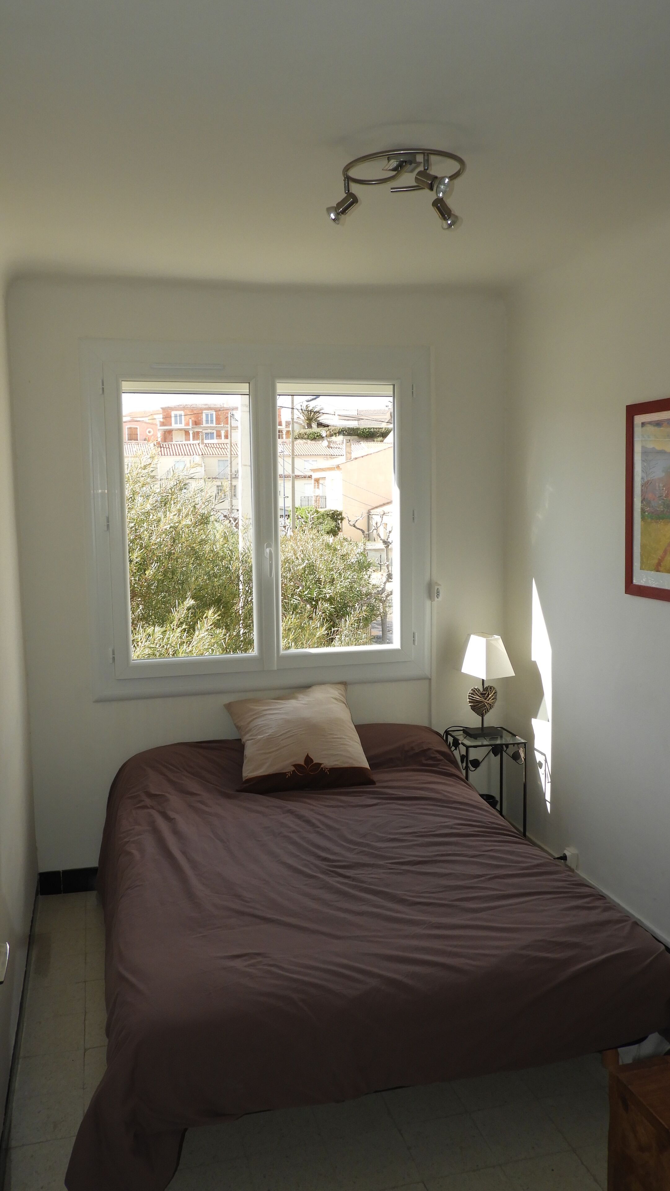 Une chambre à coucher avec un lit, une fenêtre, une lampe et un luminaire au plafond.
