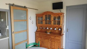 Een kamer met een houten kast met glazen deuren, een groene stoel en een aan de muur bevestigde televisie.