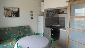 Een kleine woonruimte met een kitchenette, een bank en een eettafel.