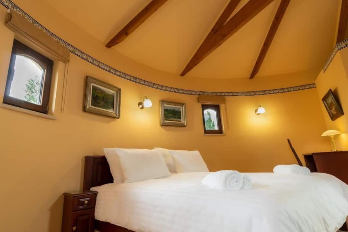 A bedroom with a large bed, wooden beams on the ceiling, and wall-mounted lights.