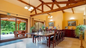 A dining area with a long wooden table and chairs, large windows, and indoor plants. - La Hacienda  (Vilvoorde)