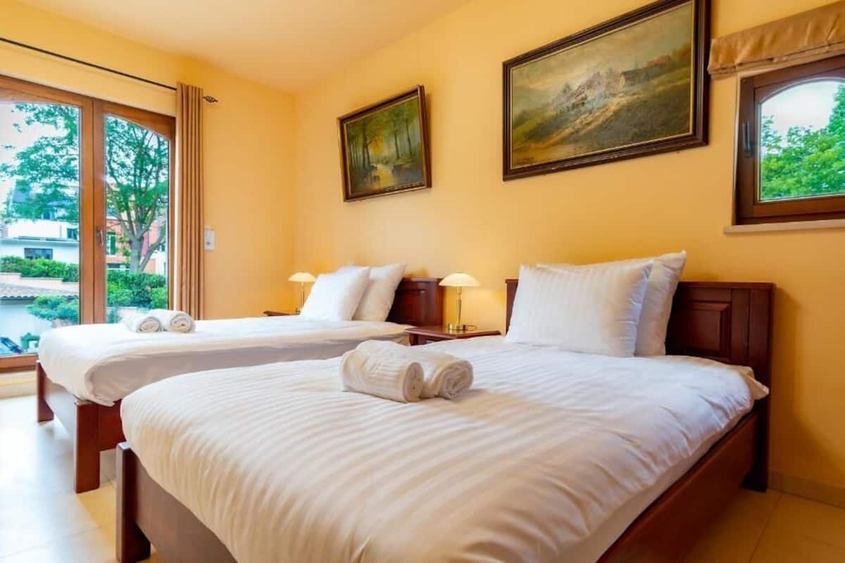A hotel room with two beds, a large window, and a painting on the wall.