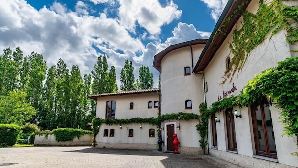 A courtyard with a building featuring a curved facade and ivy-covered walls. - La Hacienda  (Vilvoorde)