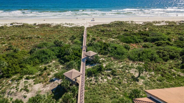 Blick auf einen Strand mit einer Holzpromenade, die zu einem kleinen Gebäude führt.