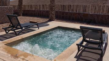 Relax by the serene pool, surrounded by a thatched umbrella and a palm tree, with lounge chairs facing the water.