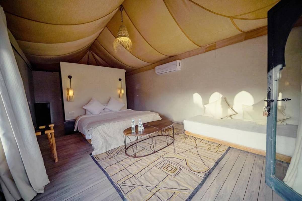 A tented room with a bed, bedside table, and a large window.