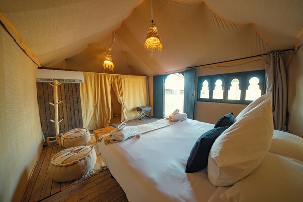 A tented room with a large bed, hanging lights, a wooden floor, and a window with curtains. - Le Bedouin Agafay (Agafay)