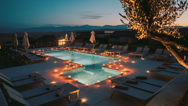 A poolside area with lounge chairs and umbrellas, surrounded by a pool with candles. - Le Bedouin Agafay (Agafay)