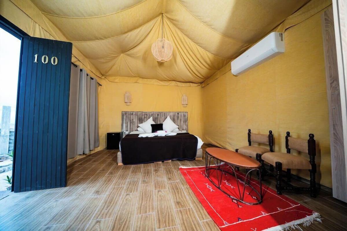 A room with a bed, a desk, two chairs, a red rug, and a tent-like ceiling.