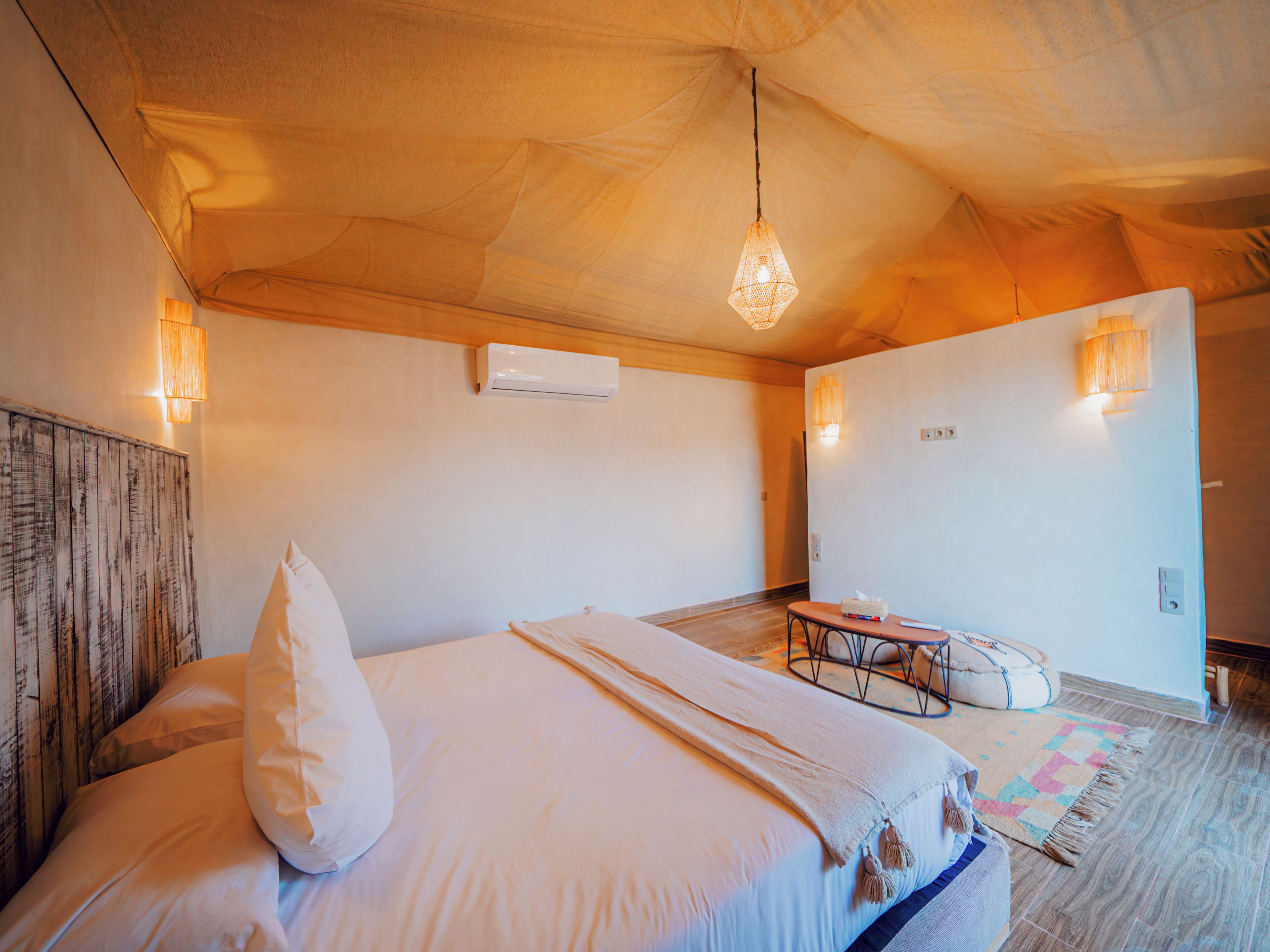 Un dormitorio acogedor con cama, cabecera de madera, lámpara colgante y aire acondicionado de pared.